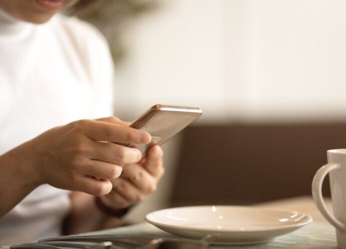 attractive smart casual female hand typing chat with smartphone tele communication with cheerful and positive attitude smile in cafe casual freelance business people concept